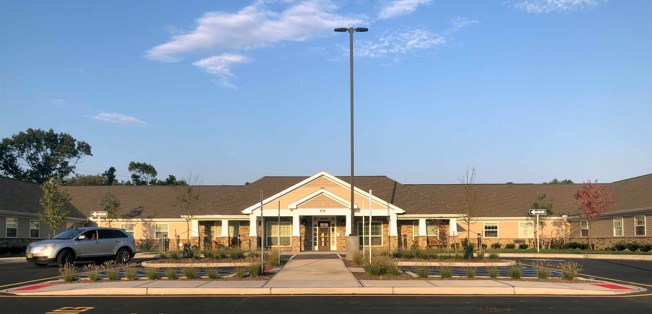 An exterior view of the Artis Senior Living single floor stone brick design building showcasing the overhang triangular design with a grass front lawn and sidewalk going across it.
