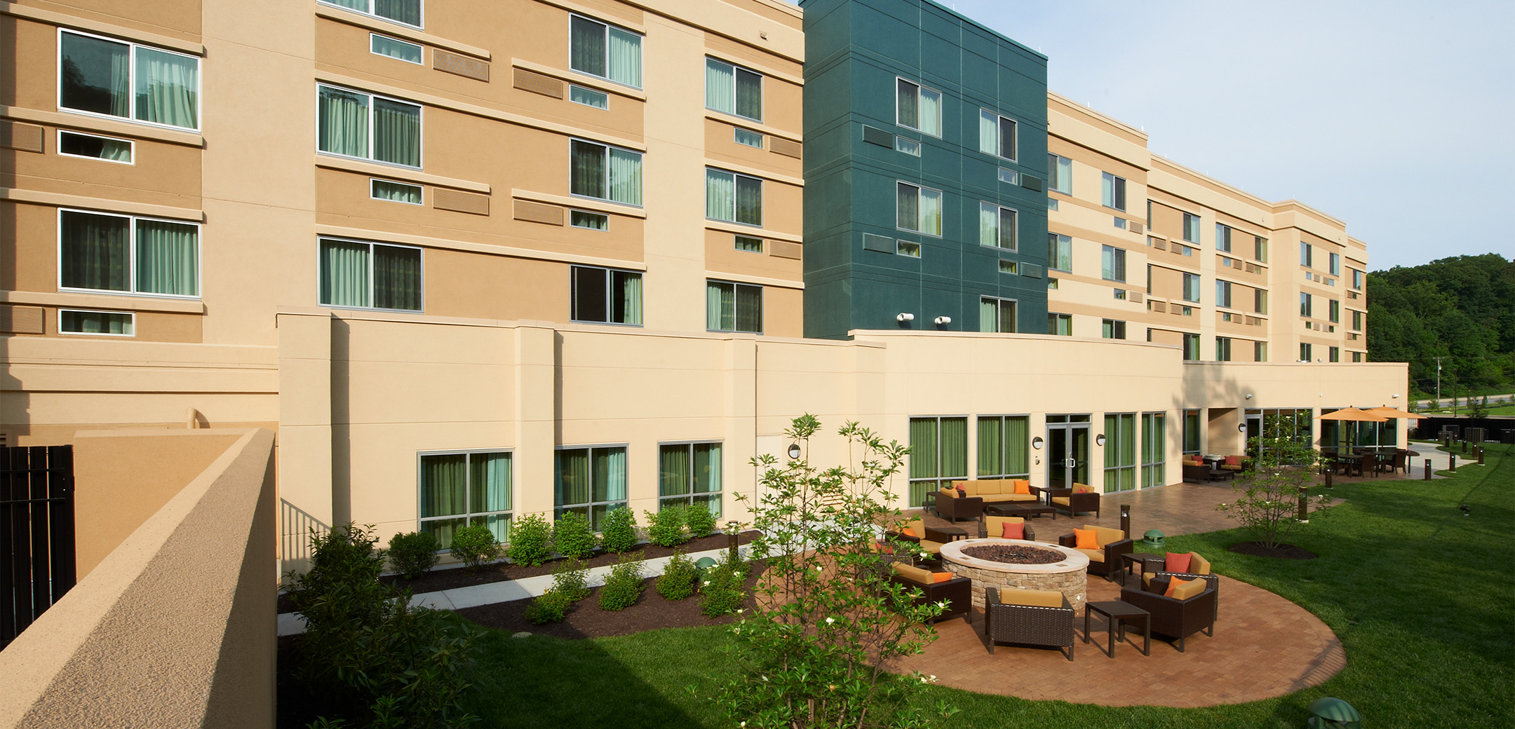 A close up of the Marriot Courtyard hotel back side showcasing the courtyard with outdoor firepits and seating areas on the first floor patio, near the grass lawn.