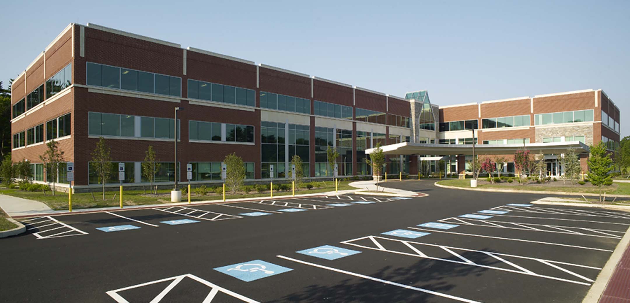 An angled view of the Main Line Health building front side, showcasing the driveway up to the entrance and large wheelchair accessible parking lot.