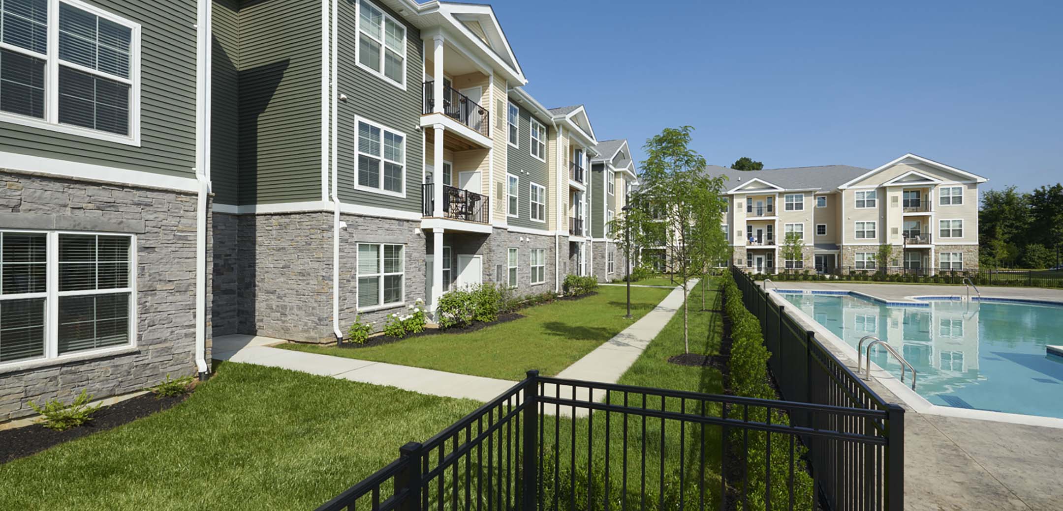 An angled view of the Signature Place MtLaurel apartment building showcasing the back courtyard with paved grass walkways and outdoor pool.