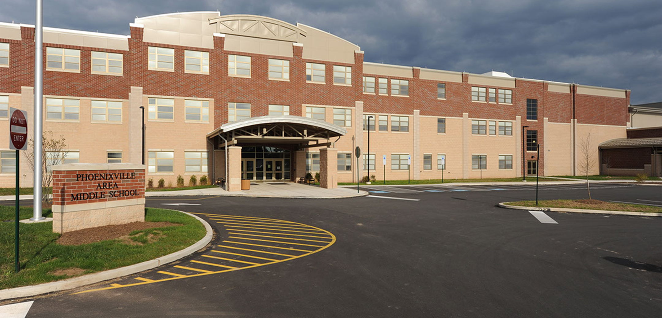 The exterior of the Phoenixville Middle School brick building showcasing the front enterance,driveway and parking space.