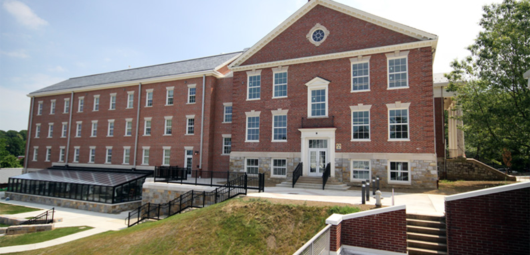 An angled view of the Merner Pfeiffer Hall of Science building's side, showcasing the side entrance, stairs leading to the lower level courtyard with grass in the foreground.