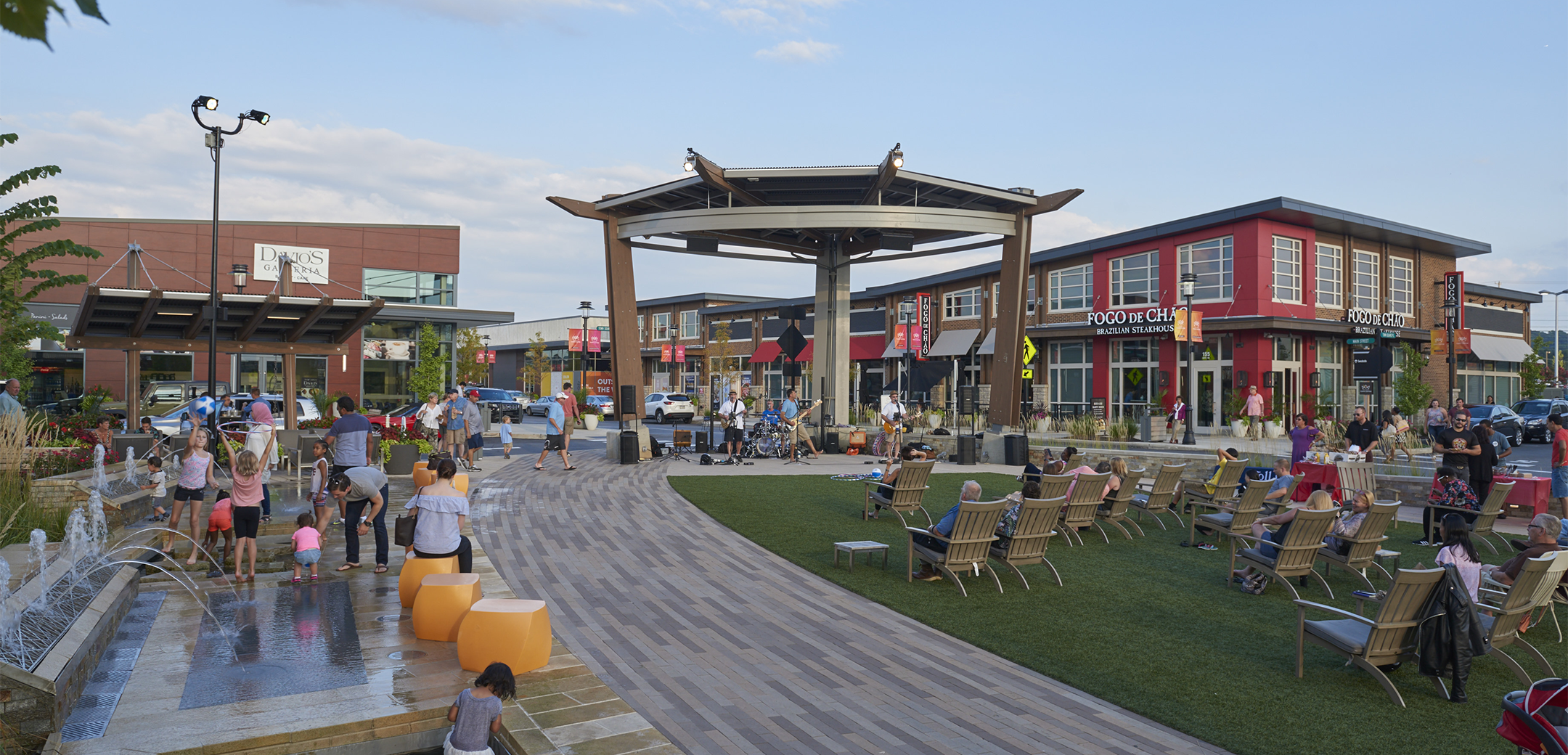 An exterior view of the KOP Center showcasing left side fountain, right side viewing and sitting area with a wooden path leading up to the stage.