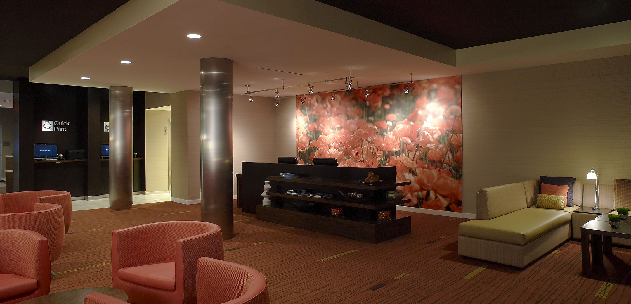 The interior of Marriot Courtyard hotel showcasing the reception desk and lobby waiting area with multiple seating areas, support pillars and a large flower background image.