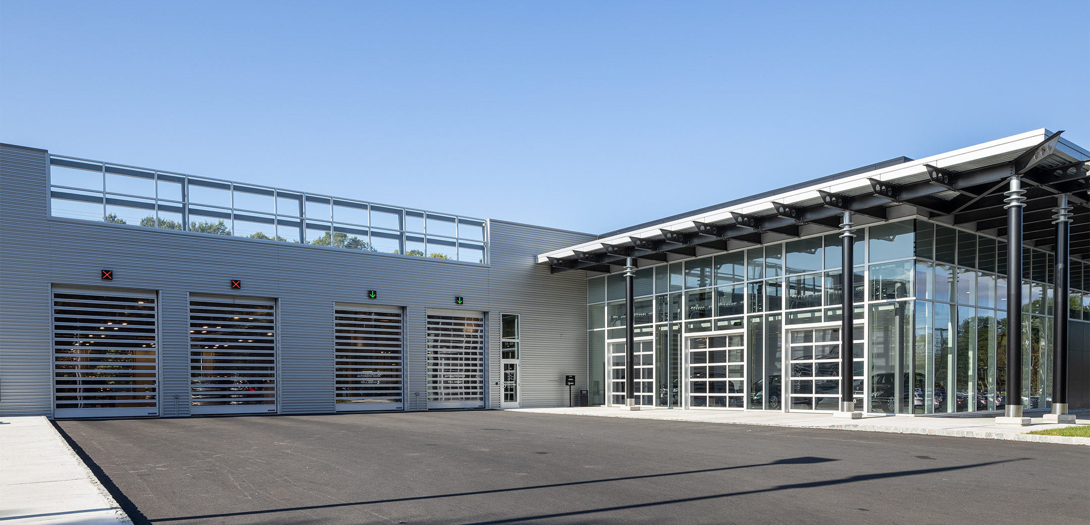 An angled view top down view of the Mercedes Benz of Caldwell glass wall building showcasing the front logo sign in the foreground, parking lot and driveway.