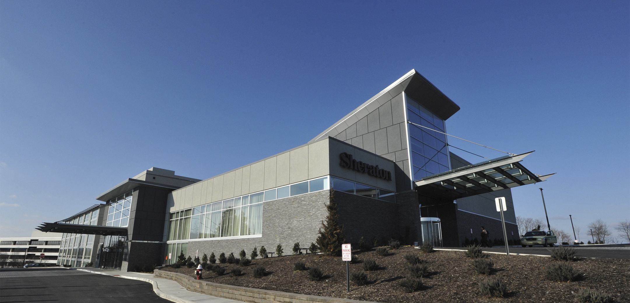 An angled view of the Sheraton Valley Forge building side entrance, showcasing their logo and entrance overhang near a landscaped area of bushes.