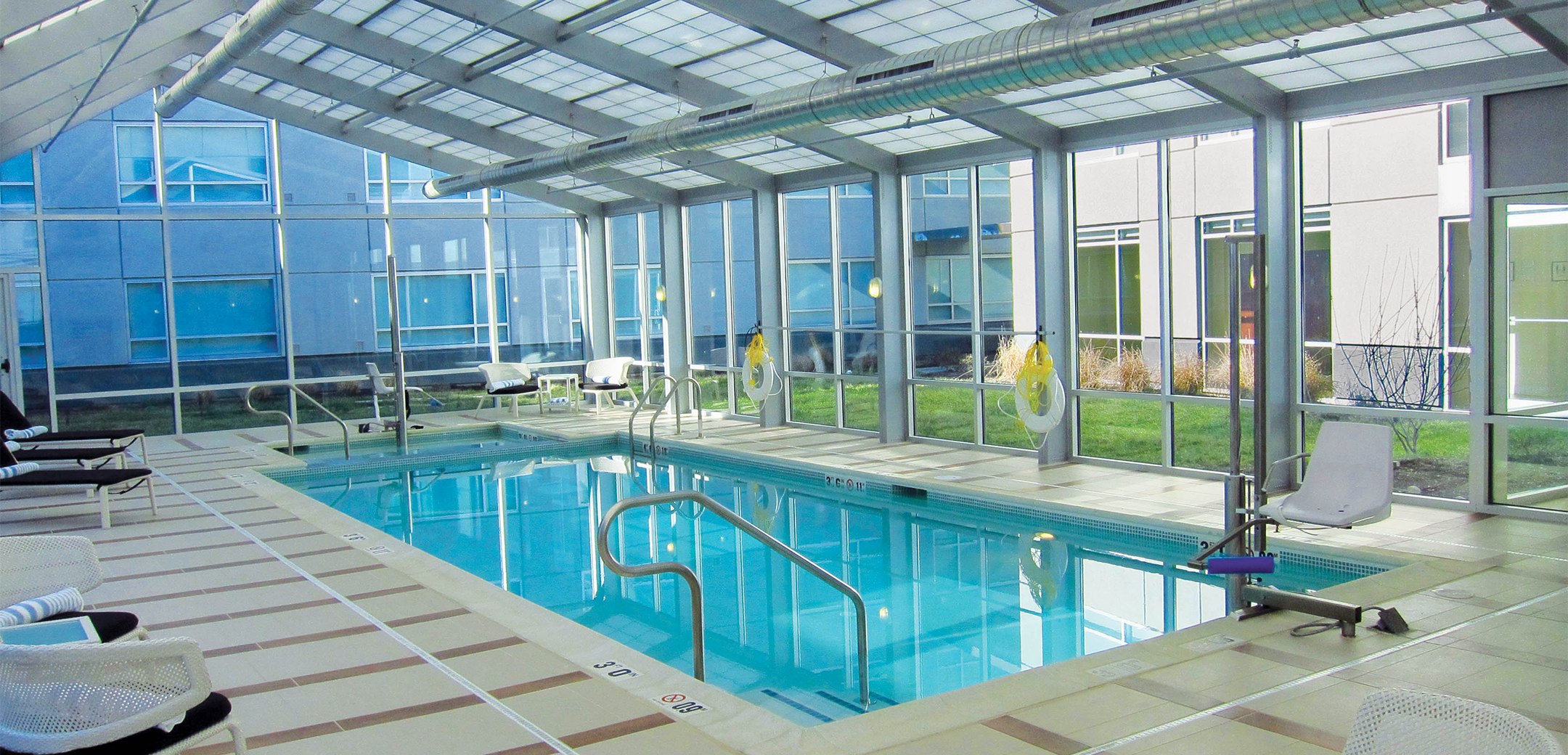 An interior of an outside glass pool house of the Sheraton Valley Forge hotel, showcasing the pool and seating area around it.