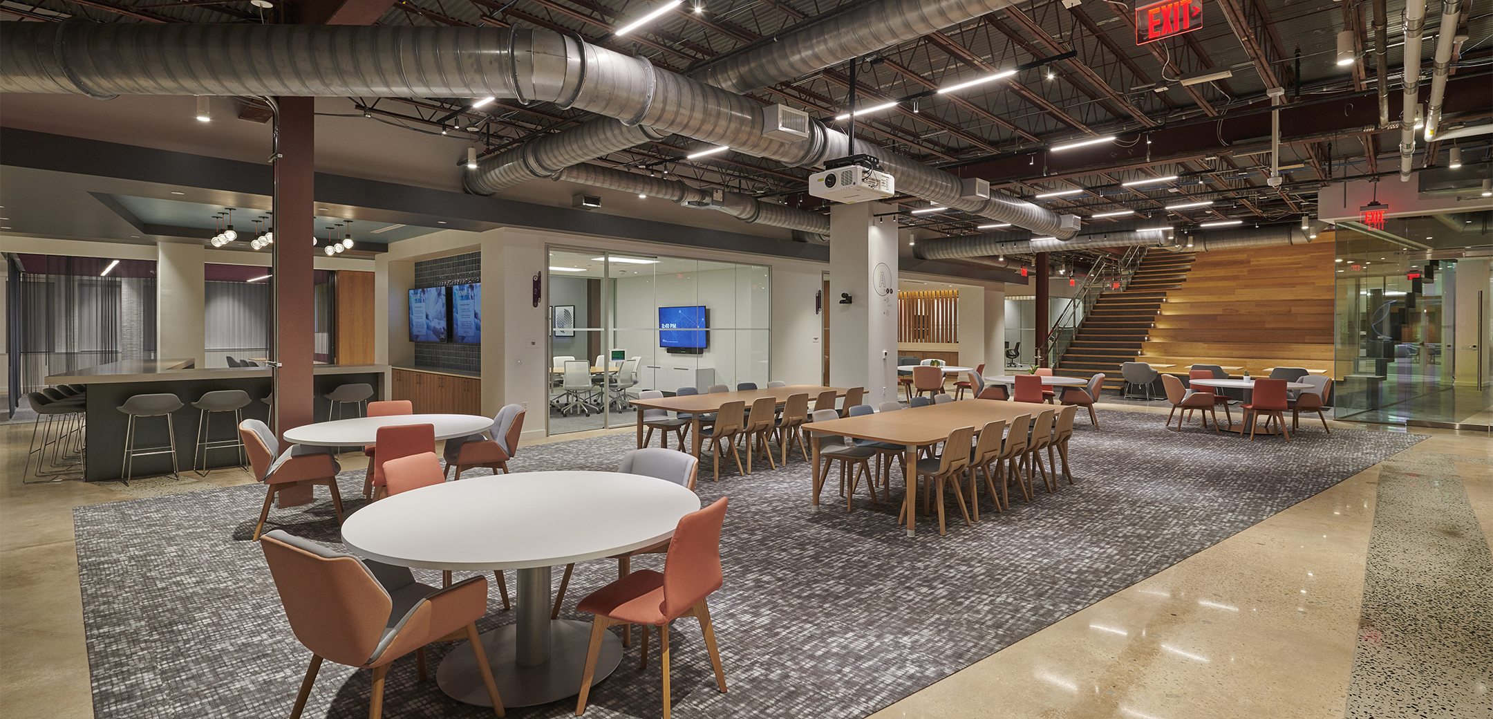 The first floor of Signant Health Headquarters featuring office furniture, conference rooms and the wide communiction staircase in the background.
