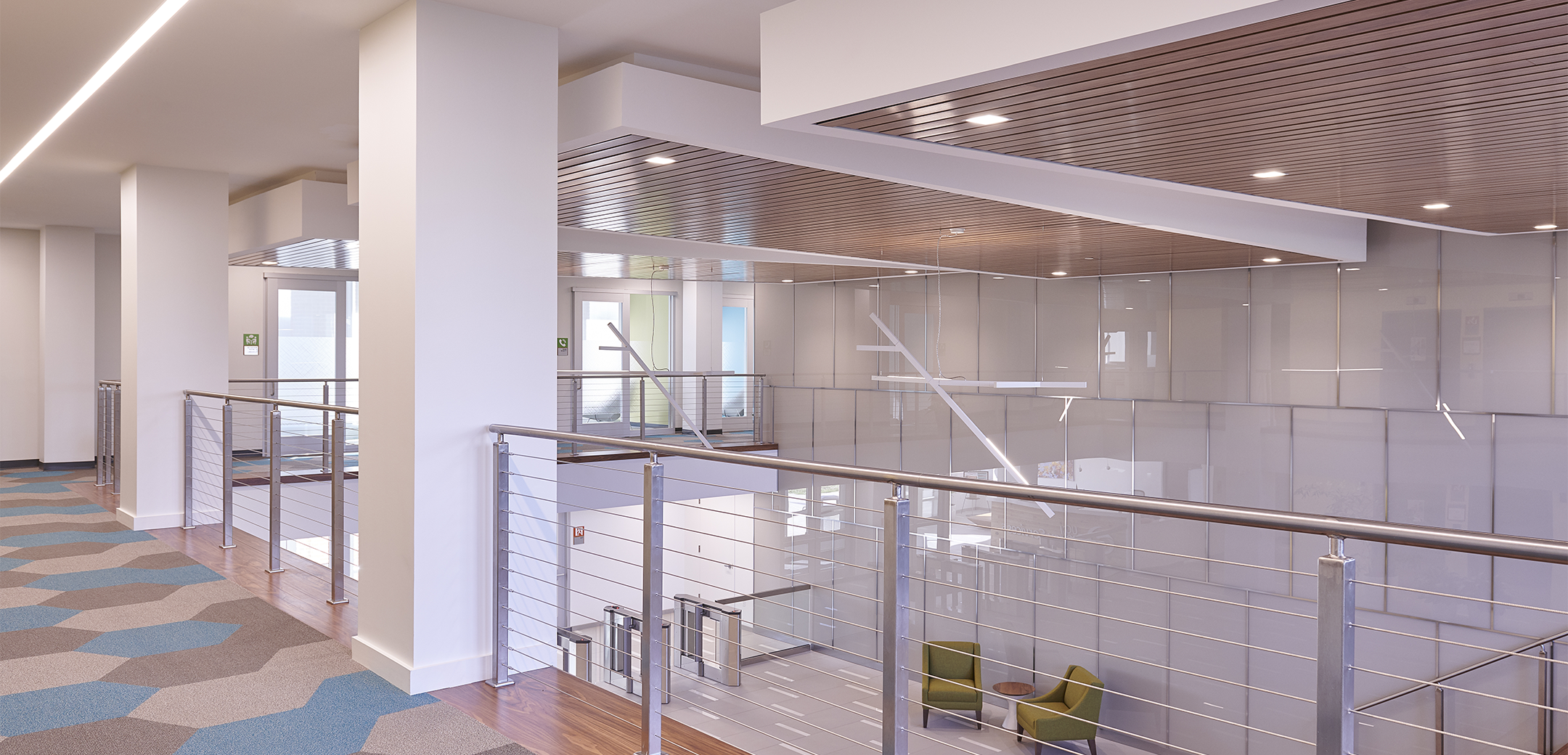 An angled view from the second floor of UGI Energy Services overlooking the first floor lobby with office furniture, office sercurity gates, and a staircase with wooden grandstand style seating.