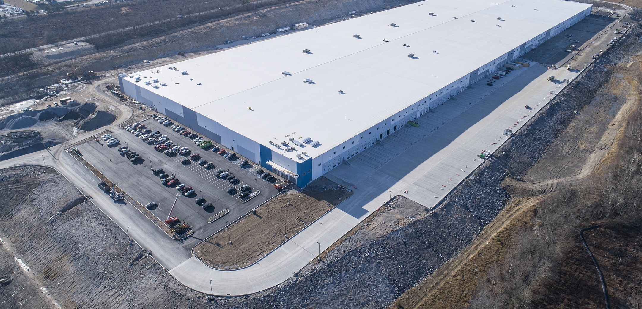 An aerial drone shot of a water bottling industrial facility with white walls and a parking lot in front with cars.