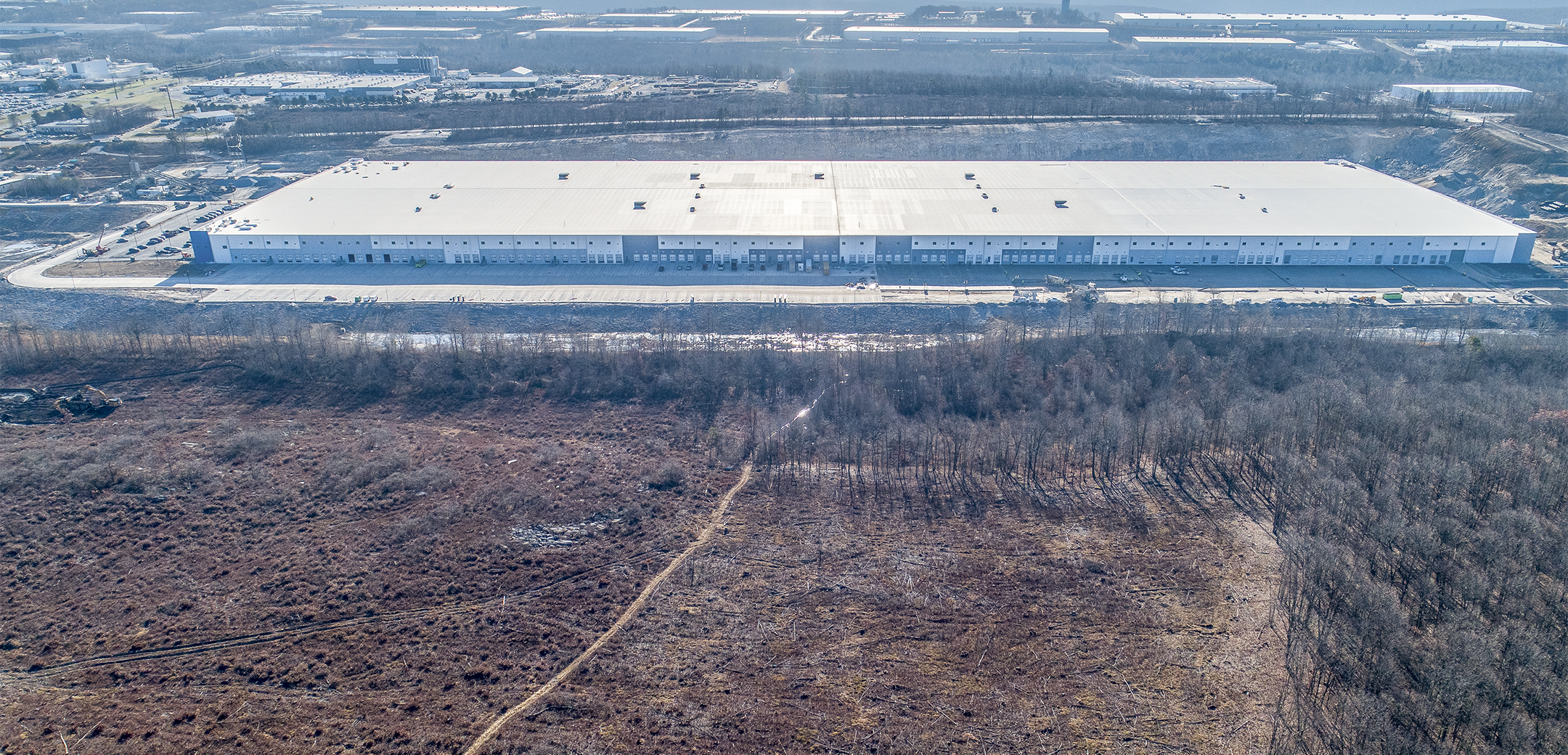 An aerial drone shot of a water bottling industrial facility with white walls surrounding by trees and landscape.